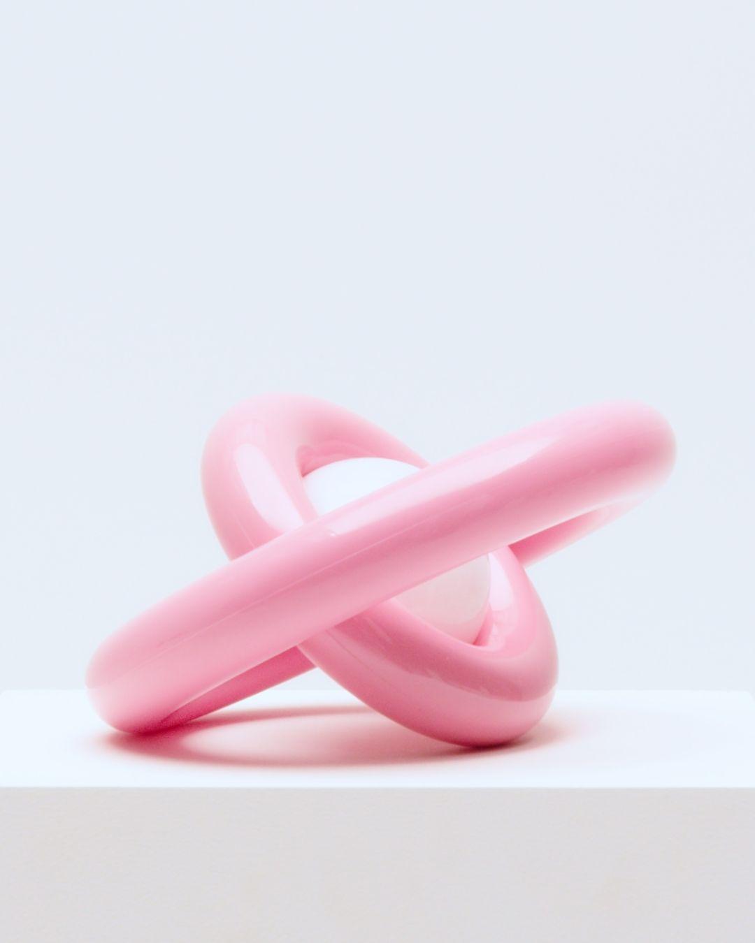 A lamp made of two intersecting pink ceramic rings with a white light in the middle of the center ring.