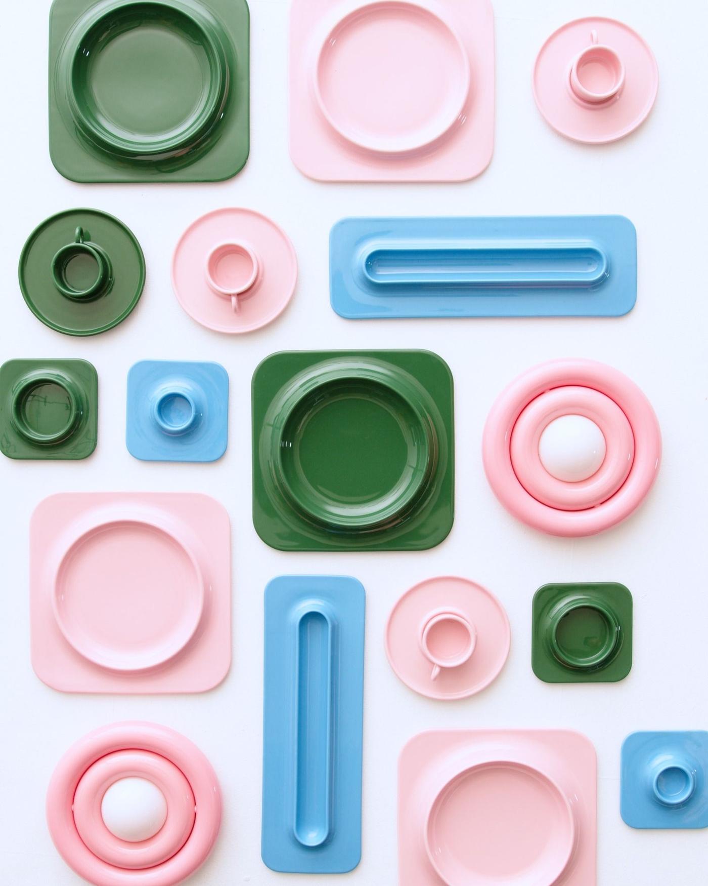 Seen from above, various coloured plates, candleholders, lights are placed next to each other on a white surface.