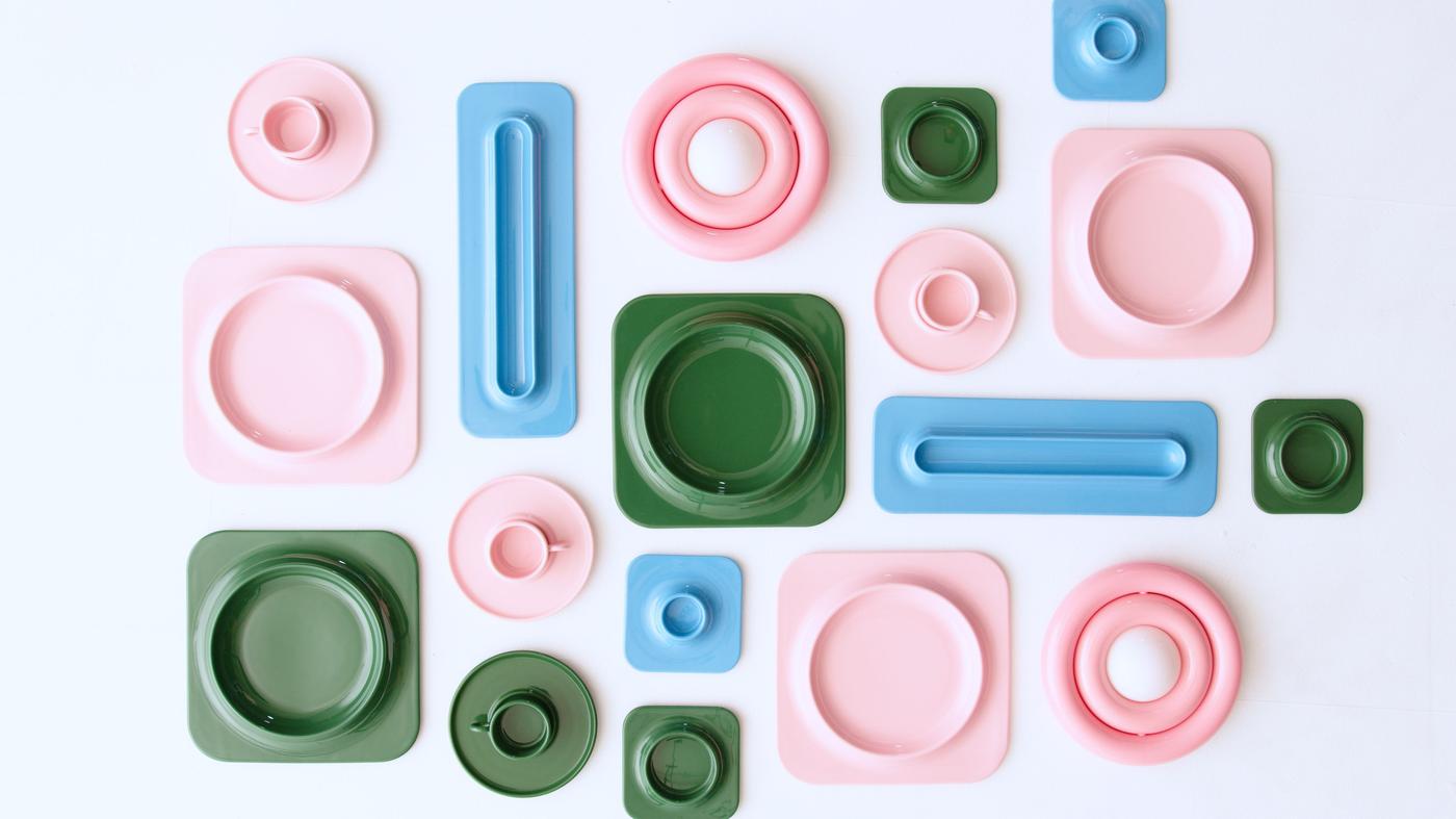 Landscape picture with plates and serving plates in green, pink, and baby blue, arranged closely like mosaics on a surface seen from above.