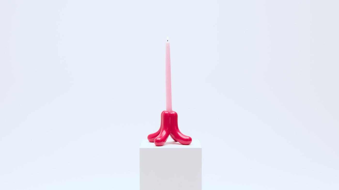 A red candlestick with a large pink pillar candle.