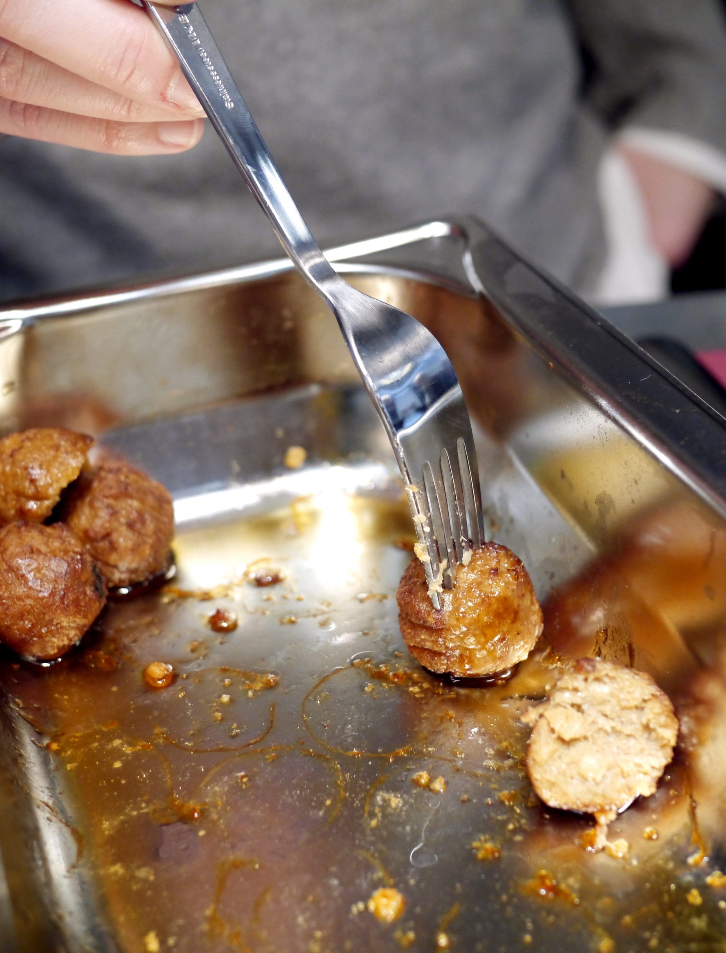 Several cooked plant balls in a stainless steel tray and a hand with a fork digging into one of them.