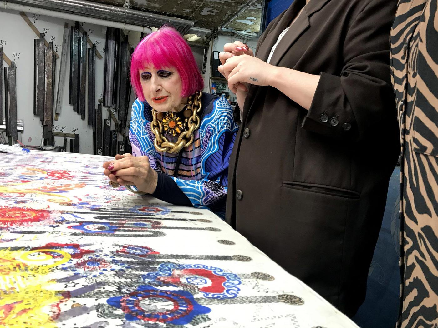 Zandra Rhodes looking at colourful prints laid out on a large table.