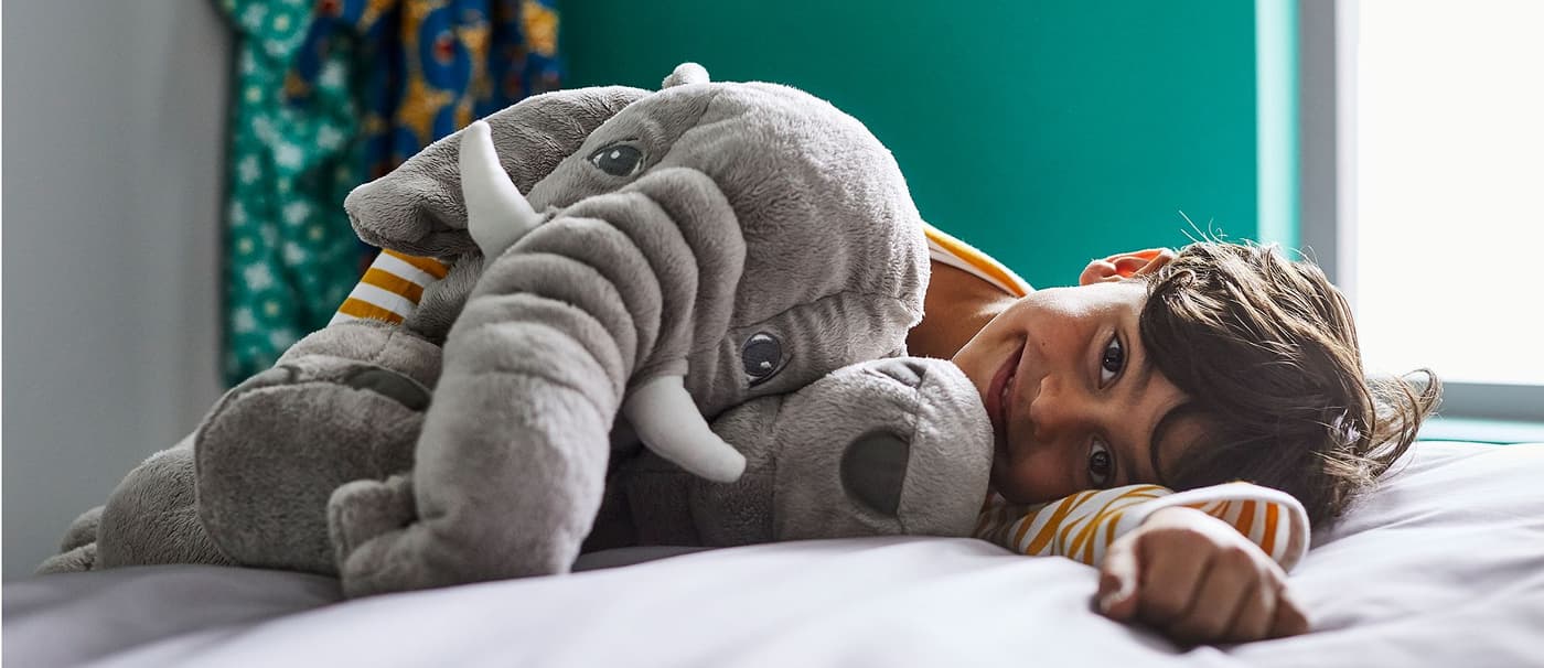 A little boy laying on a bed in his bedroom smiling with a soft toy in his arms.