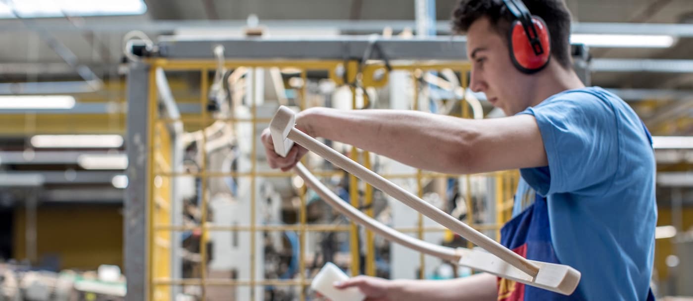 A man in a factory working with wood. He is wearing a blue t-shirt and orange noise-cancelling headphones.