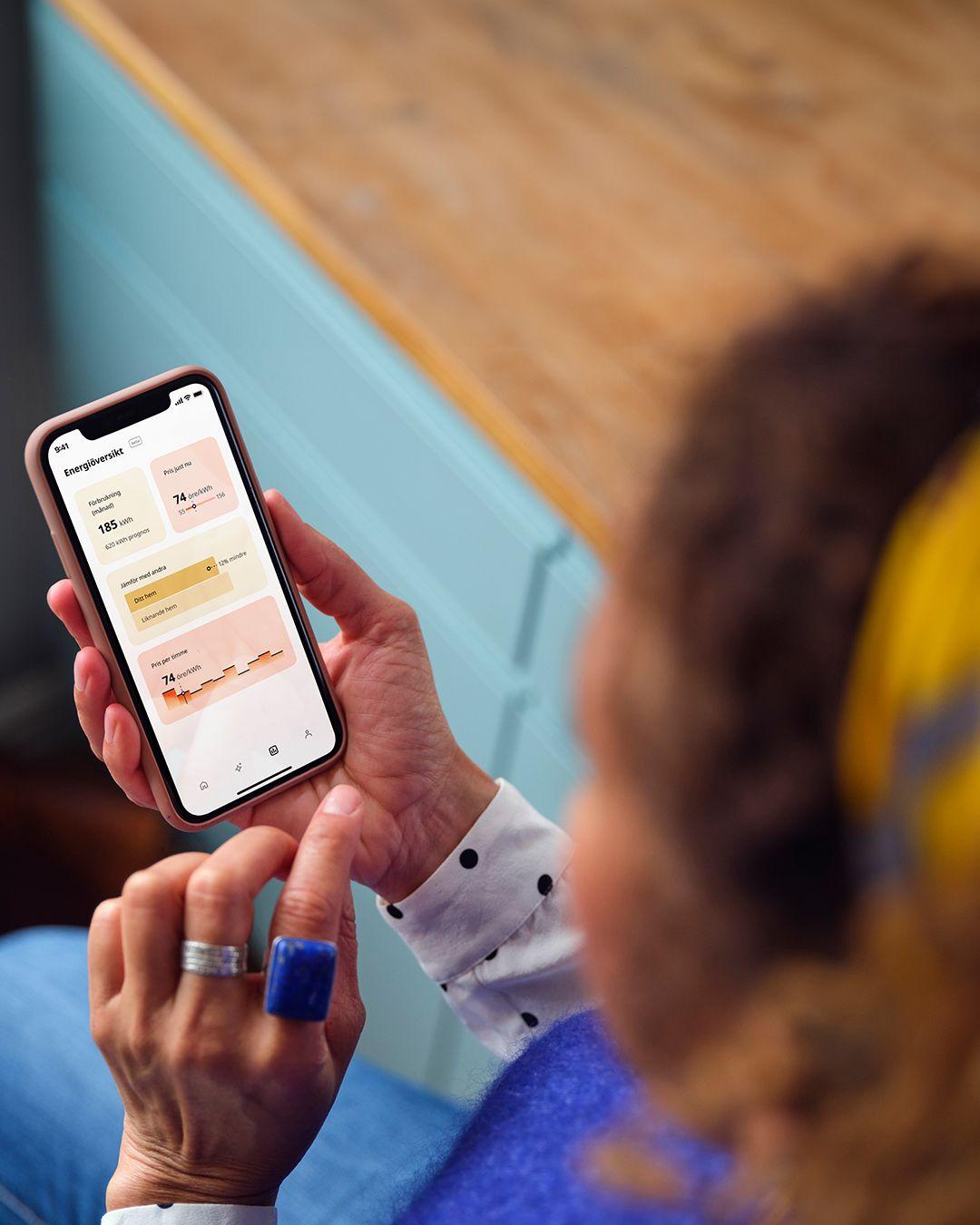 A girl with yellow headband is pointing at iphone touchscreen with her finger, playing with the new Energy Insights feature in the IKEA Home smart app