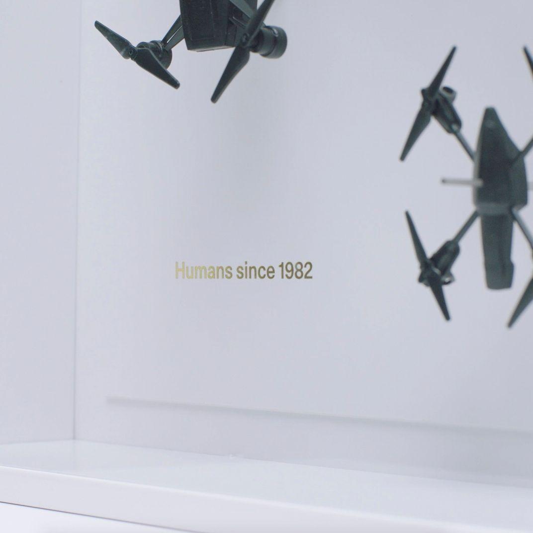 A photo print of two black drones with gold-coloured text, on a white wall above a white ledge.
