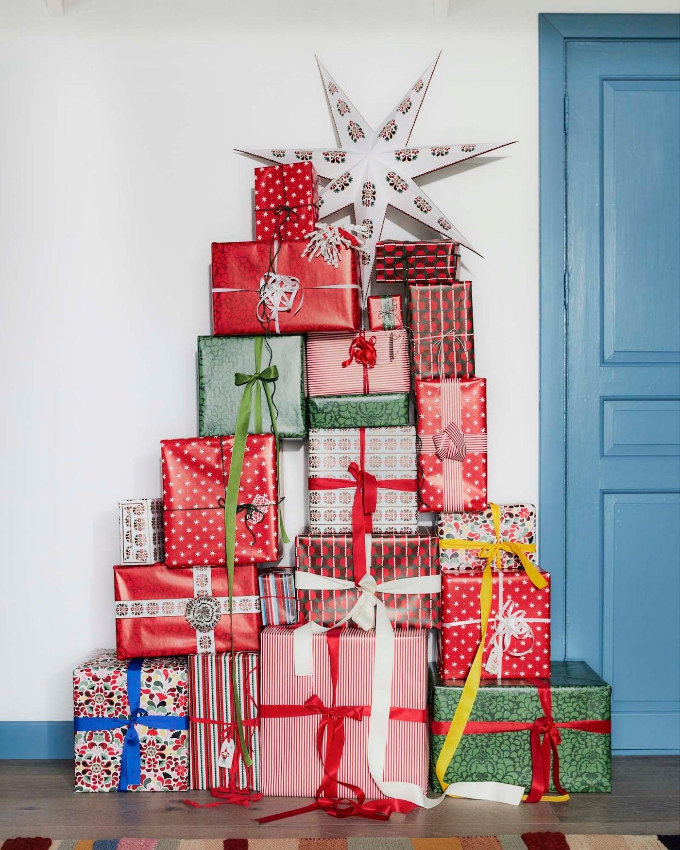 A stack of wrapped gifts against a wall in the shape of a Christmas tree.