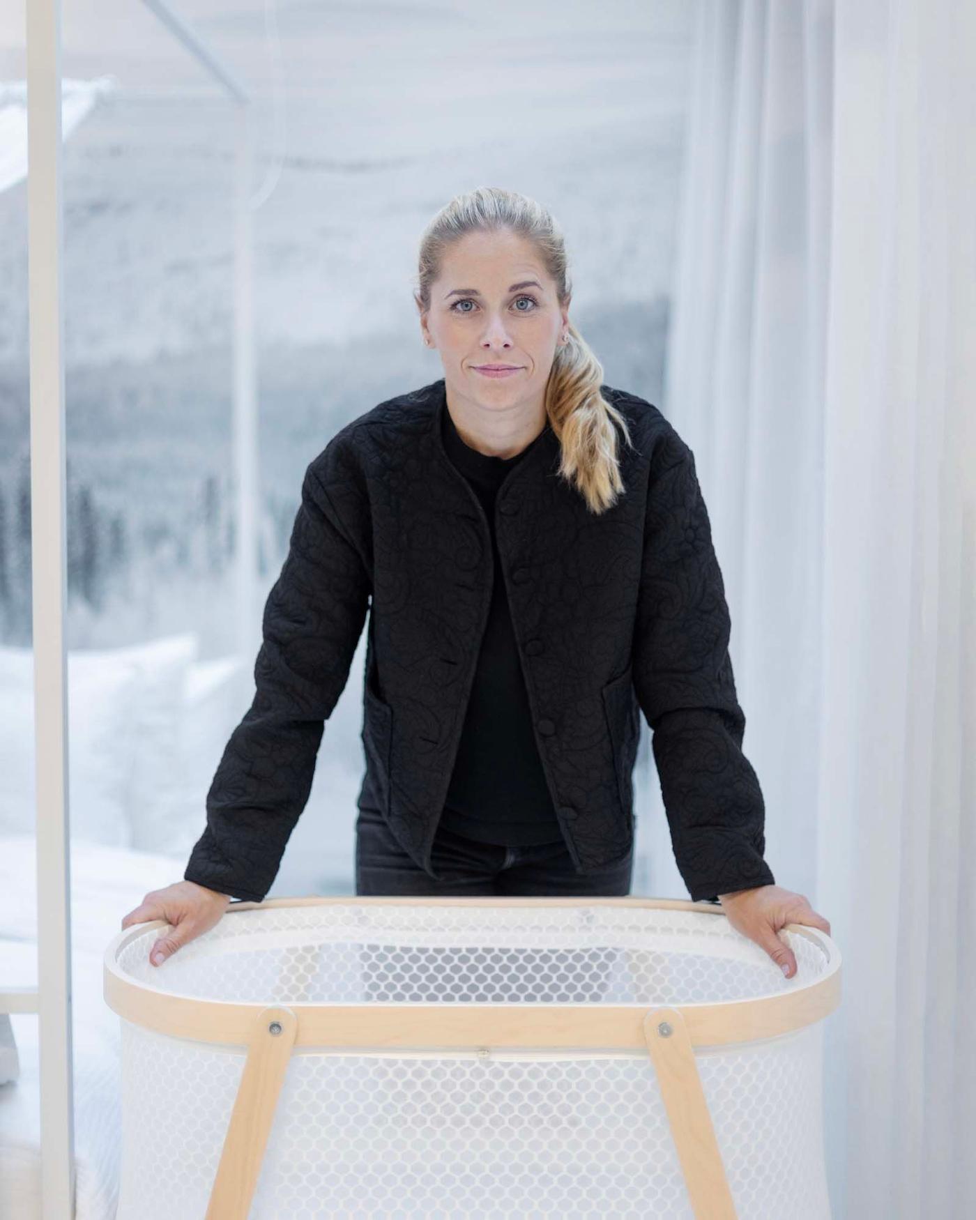IKEA designer Sarah Fager stands over a bassinet with her hands on it and looks at the camera.