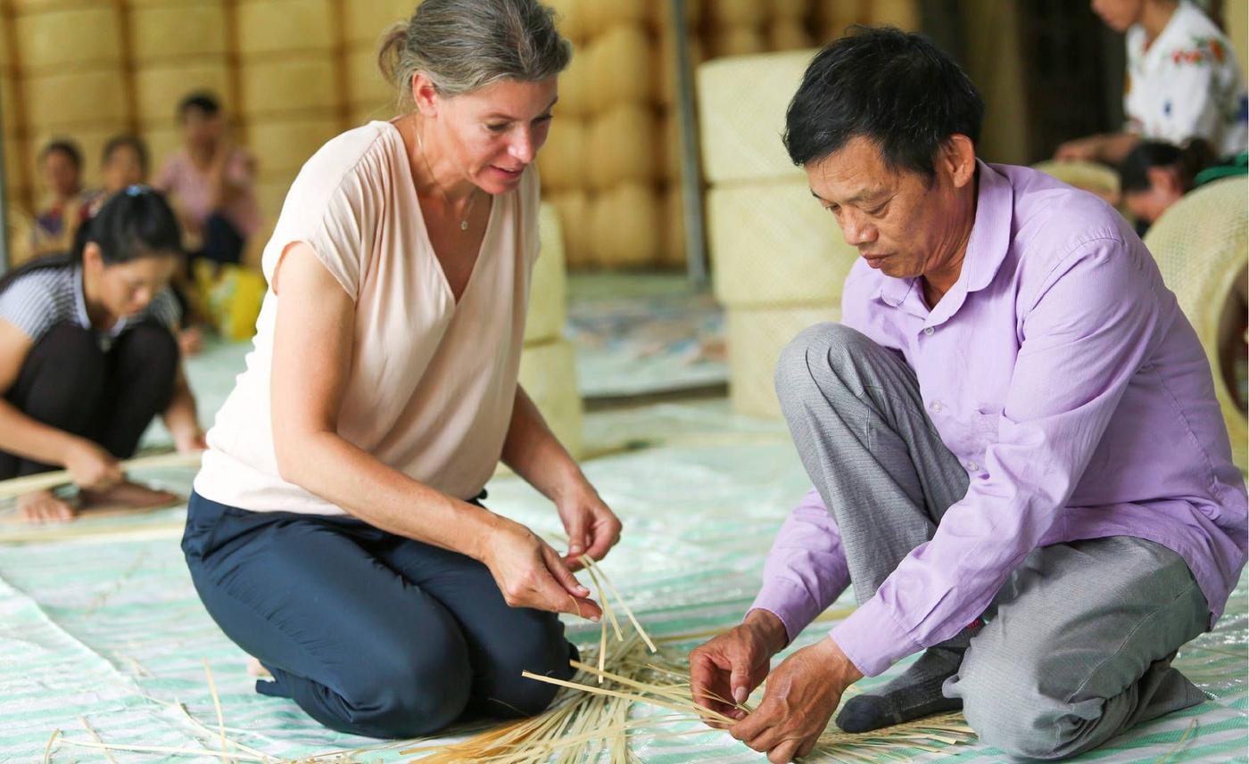 Designer Emma Olbers and an artisan crouching down in a factory in Vietnam and selecting strips of bamboo.