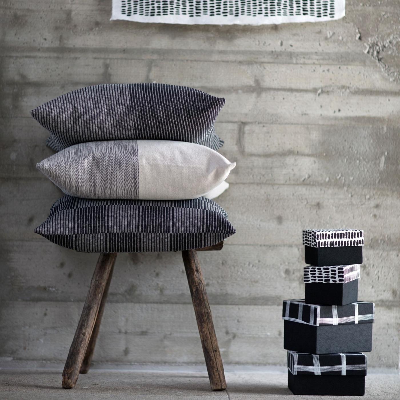 A stool and three stacked cushions with hand-woven EFTERTANKE cushion covers and four black and white handmade paper boxes.