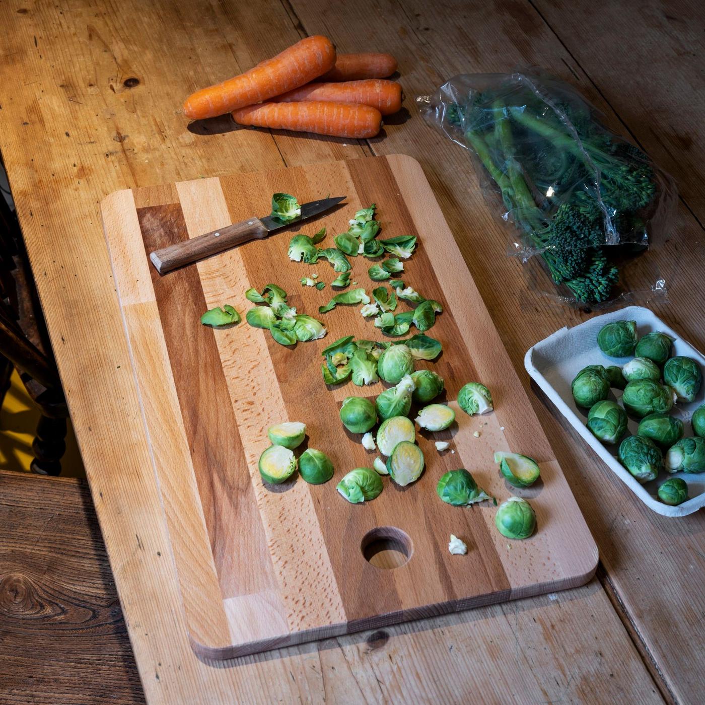 A chopping board with a knife, kale and carrots.