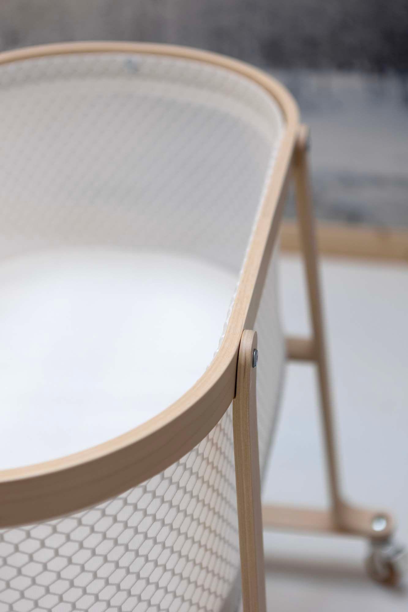 Close up of the edge of a white and light wood bassinet.