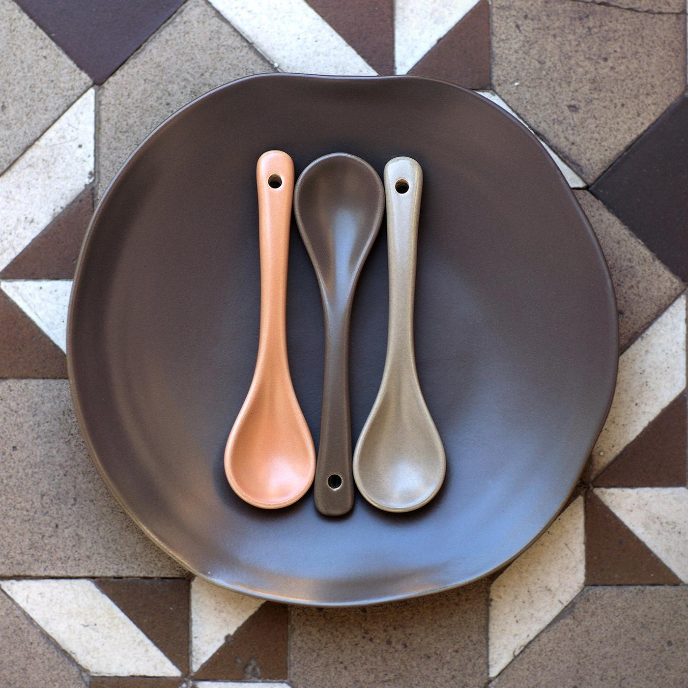 A large, dark brown FULLVIKTIG ceramic plate and three brown and grey ceramic ladles placed on a tiled floor with a graphic pattern.