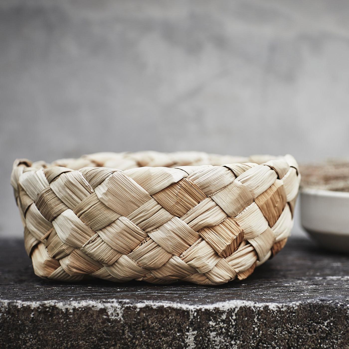 A handmade, Scandinavian-style basket from the HANTVERK collection placed on a dark grey piece of rock.