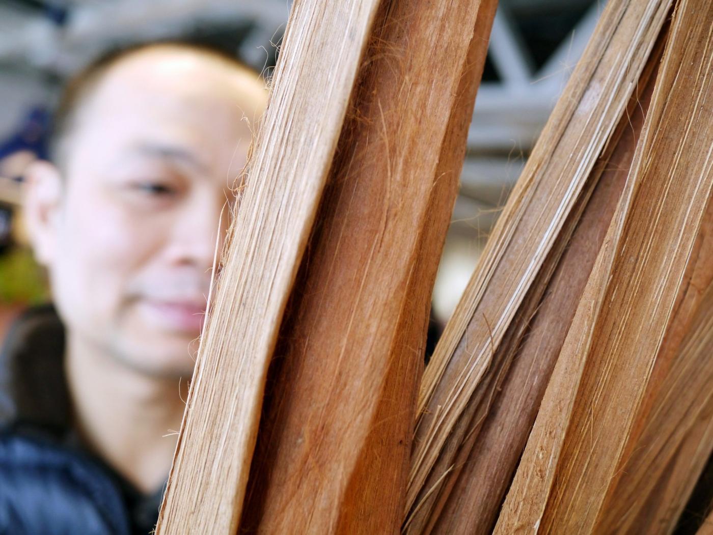 A smiling man looking at brownish nipa palm leaves.