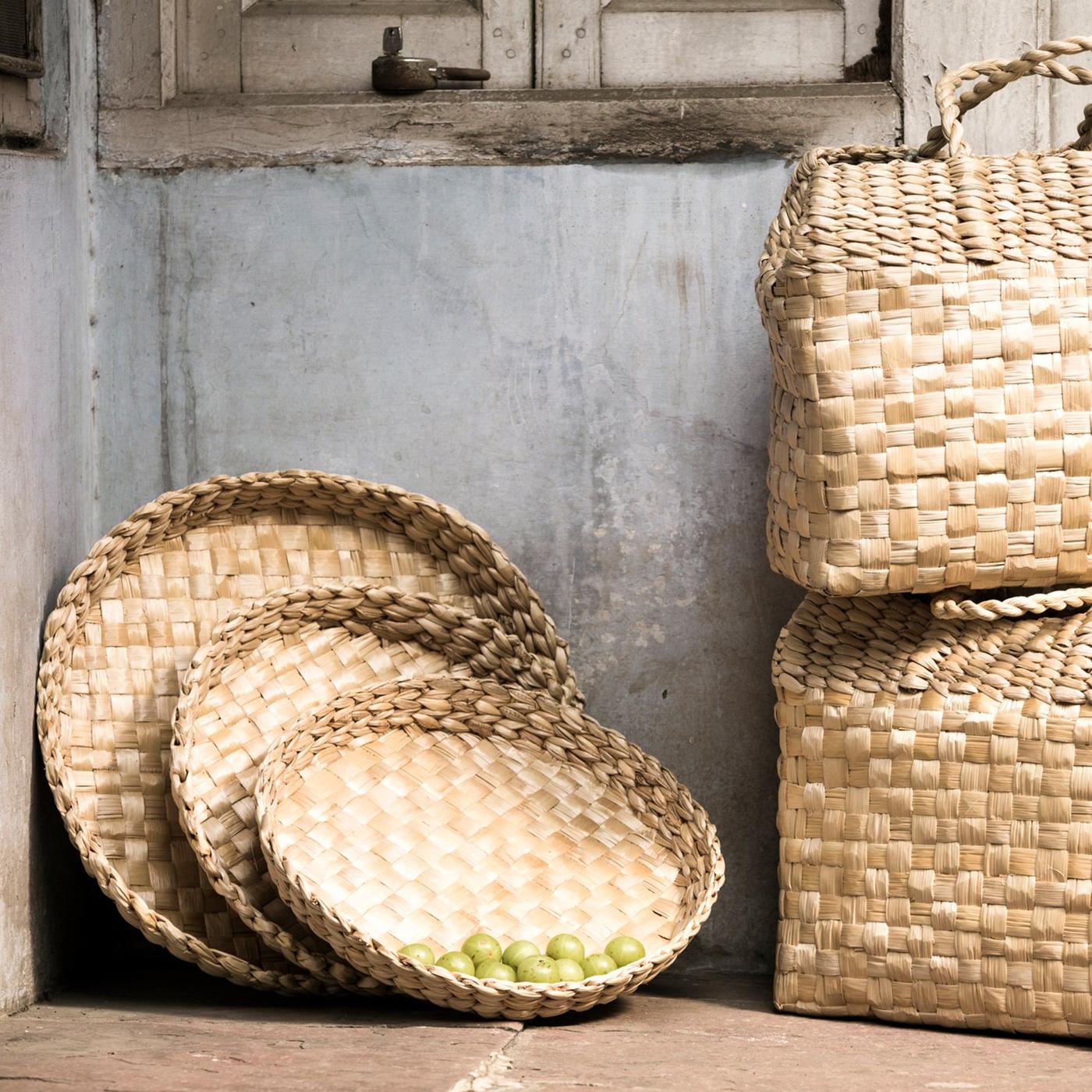 Two HEMJORD hand-woven bags and several hand-woven trays leaning against a wall, all in renewable, natural banana fibre.