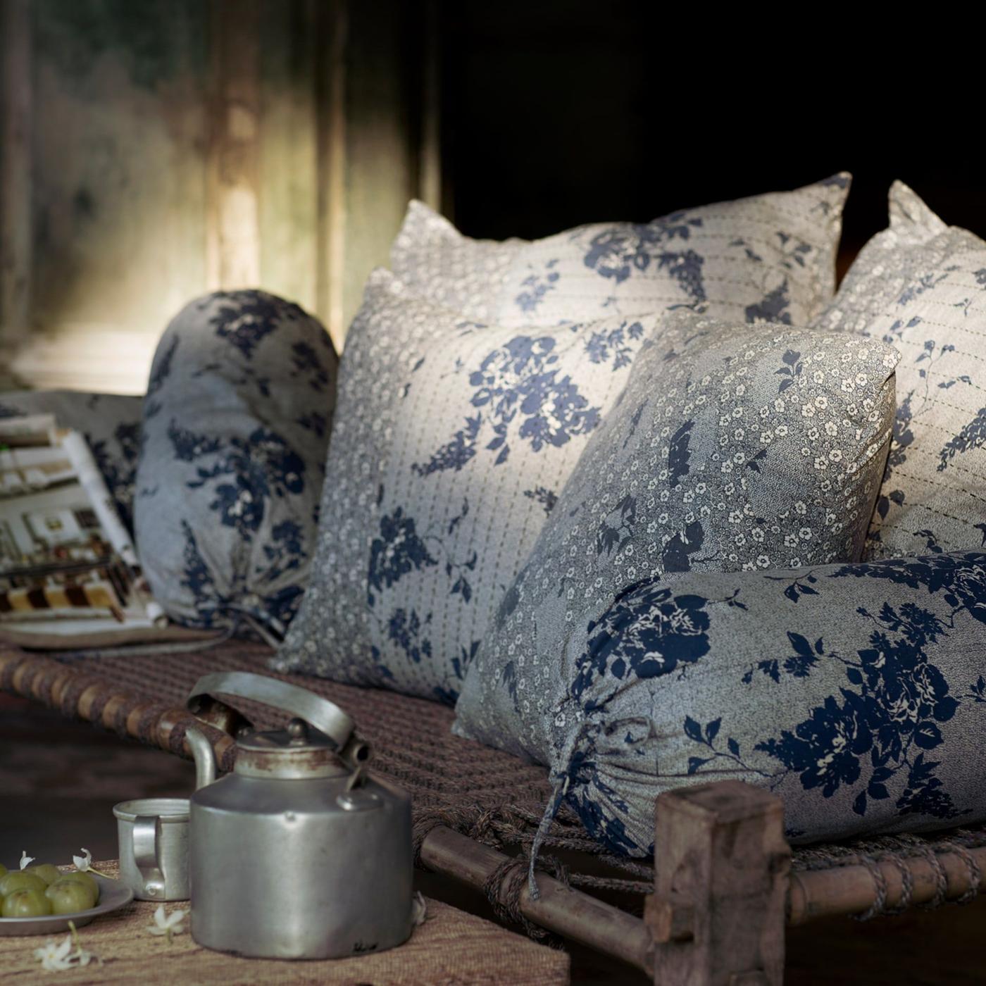 A rattan bench, cushions in various sizes and handmade HEMTRAKT cushion covers with blue floral patterns, and a tea kettle.