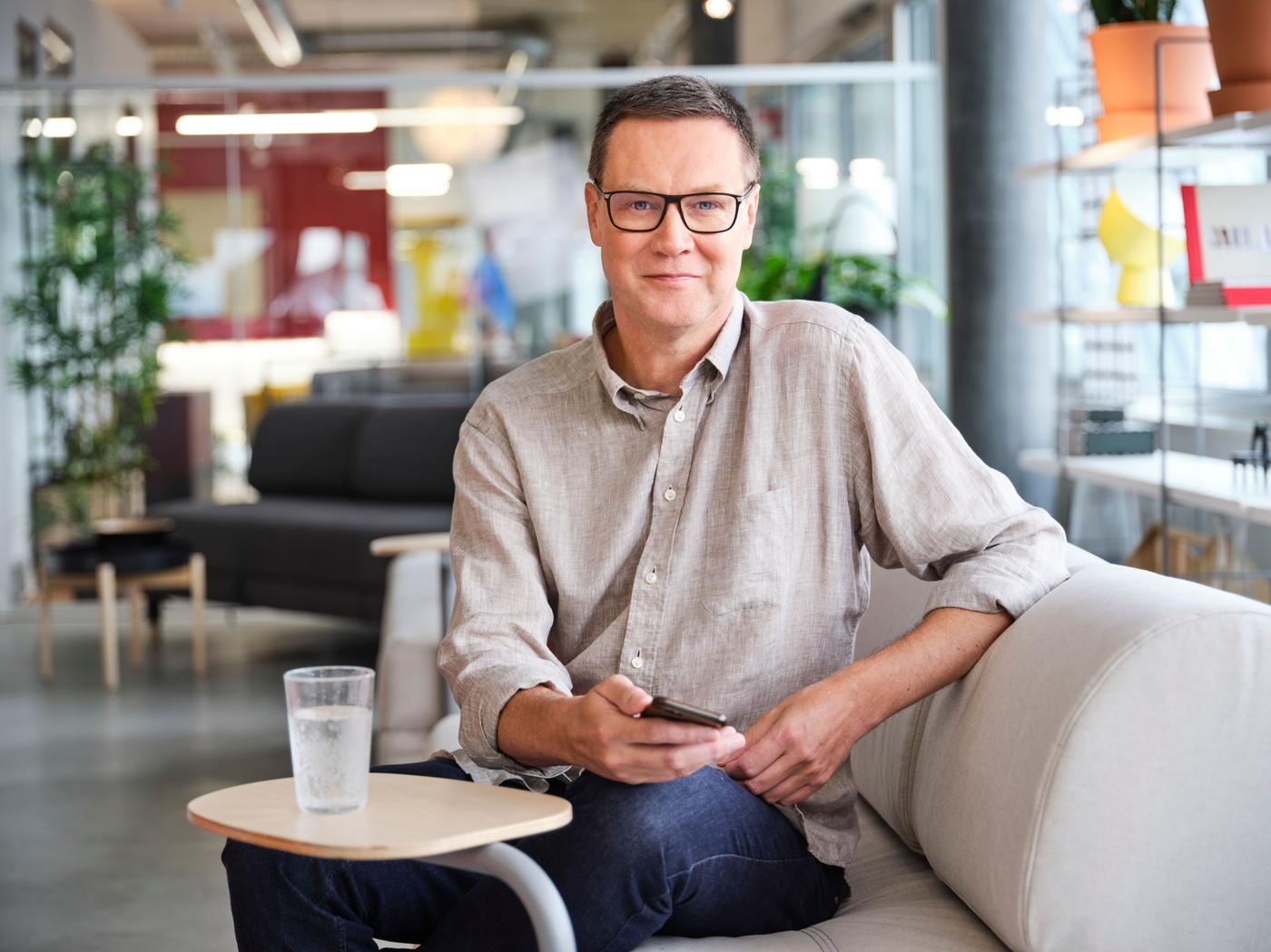 A portrait of a Henrik Elm wearing glasses and a beige shirt, seated in an IKEA office.