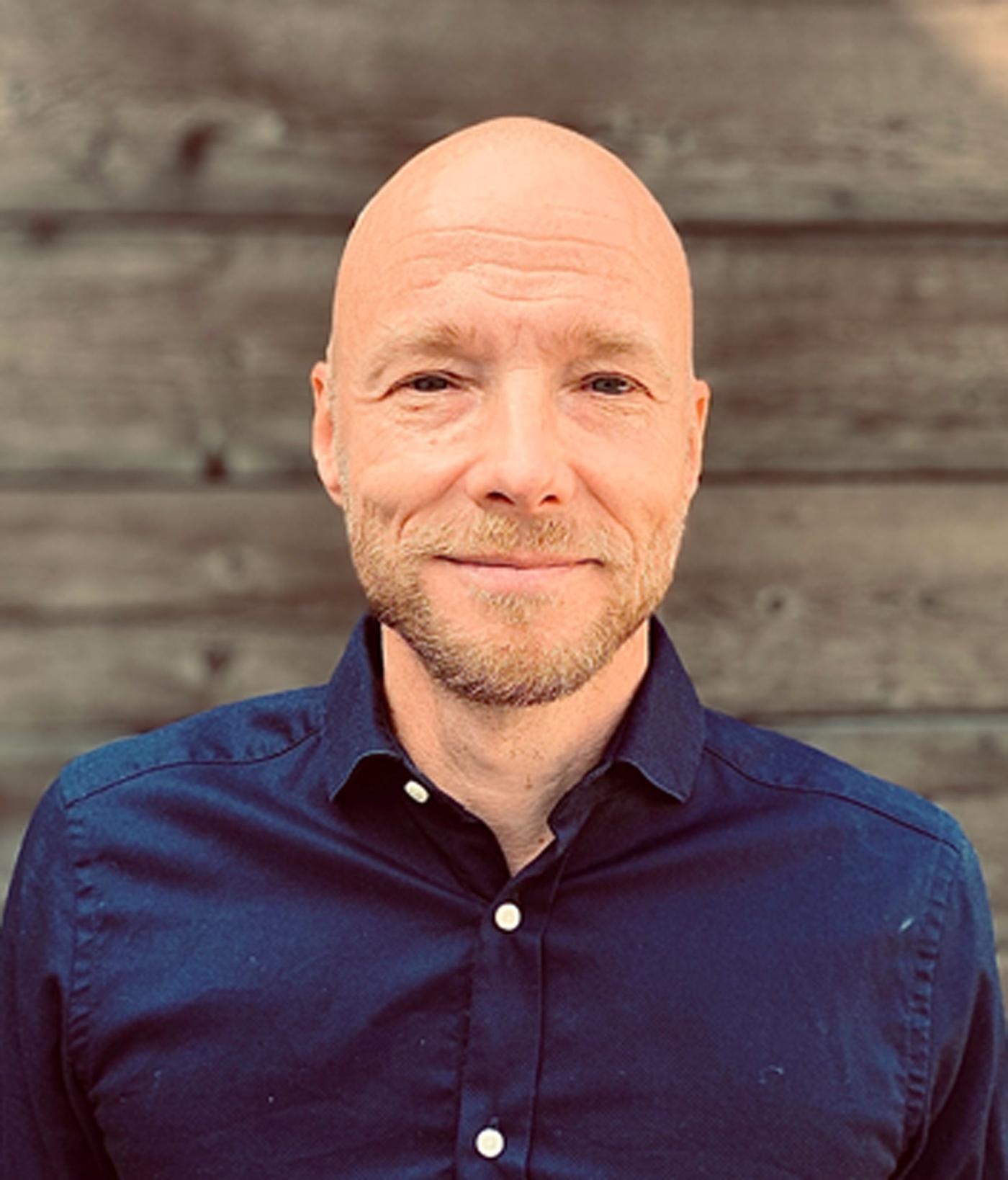 Henrik Telander, product owner for IKEA of Sweden, in a blue shirt and standing in front of a dark wooden wall.