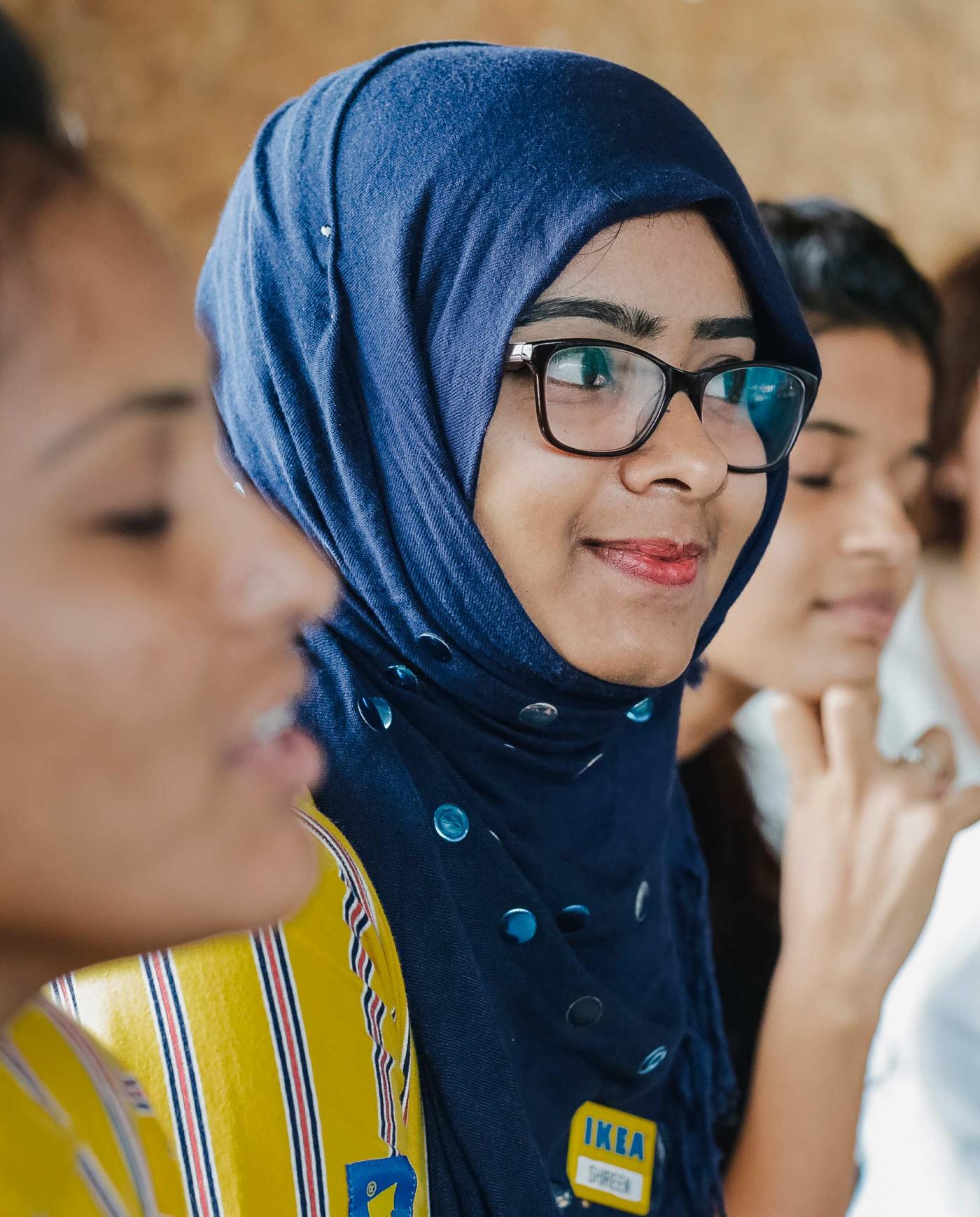 Portrait of the face of Shireen Begum who is working at IKEA in Hyderabad. She wears black glasses and a blue hijab.