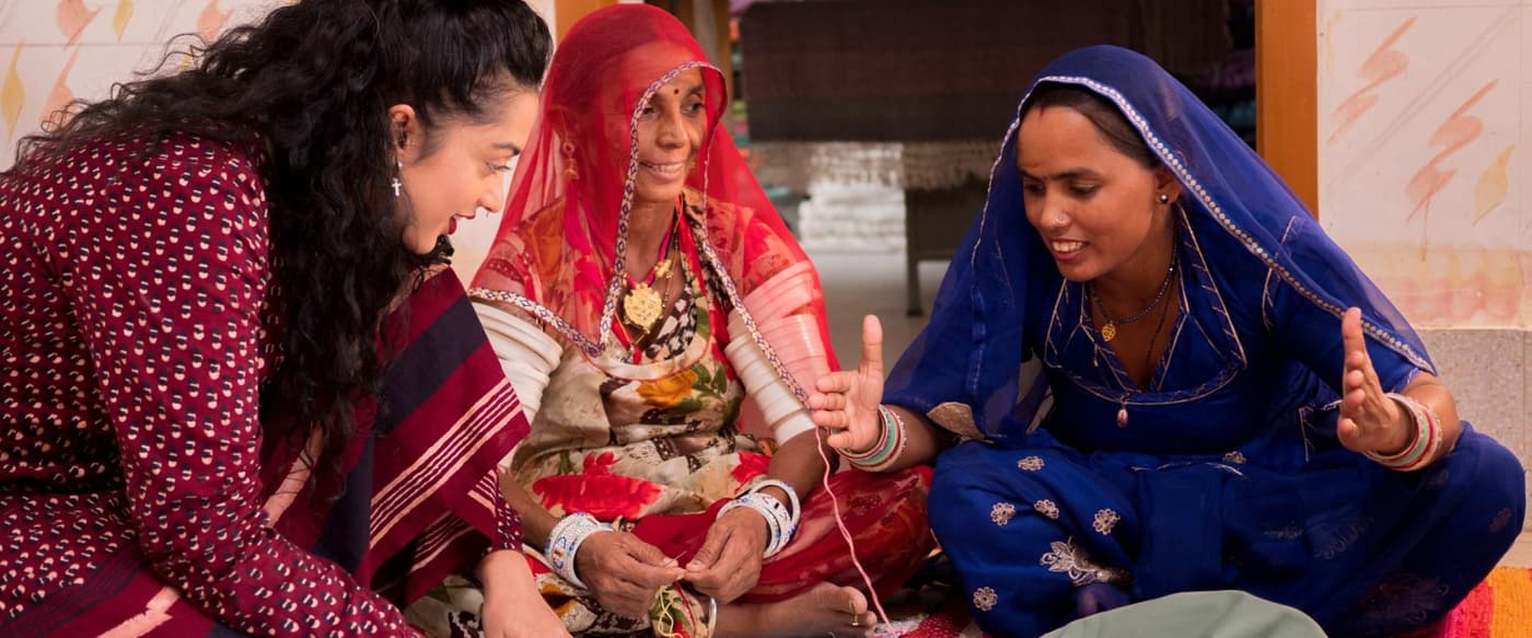 IKEA designer Akanksha Deo and two artisans in colourful, decorative dresses are sitting on the floor while talking.