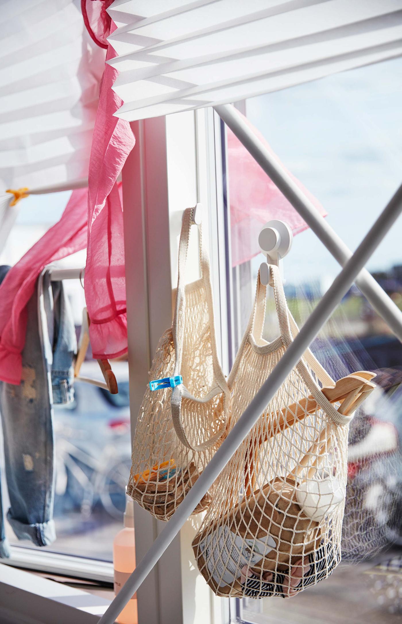 Two IKEA KUNGSFORS net bags in beige cotton from more sustainable sources hanging in a window.