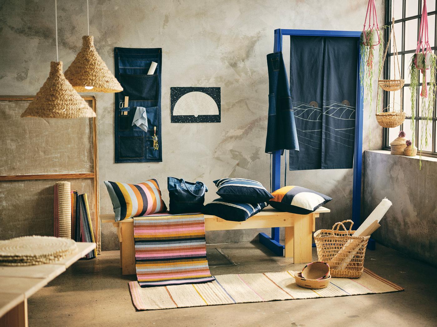 A room setting with home furnishing products in natural fibres and denim hanging on the wall and lying on a bench. 