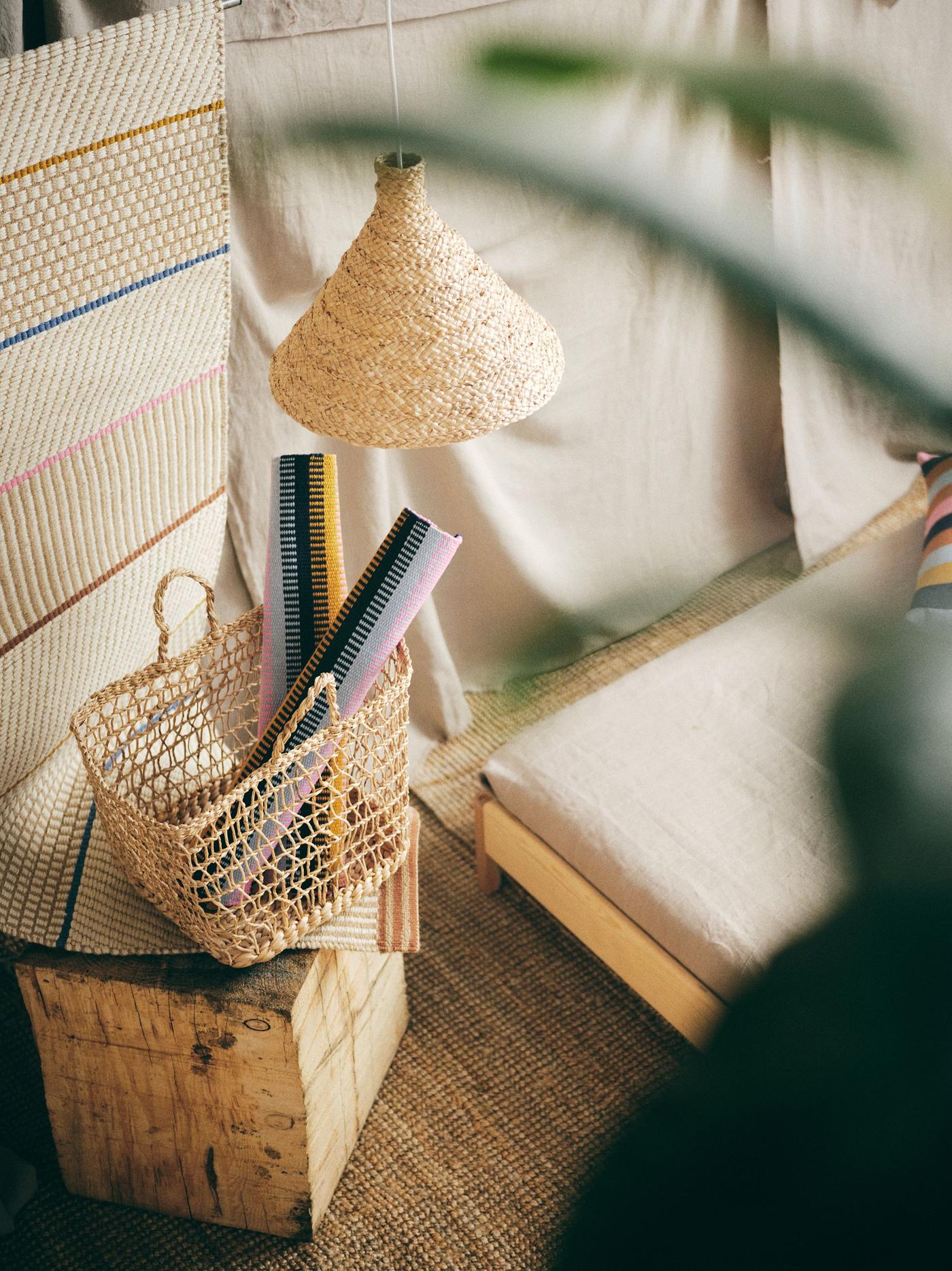 A handmade basket with two rolled up rugs standing on a wooden box.