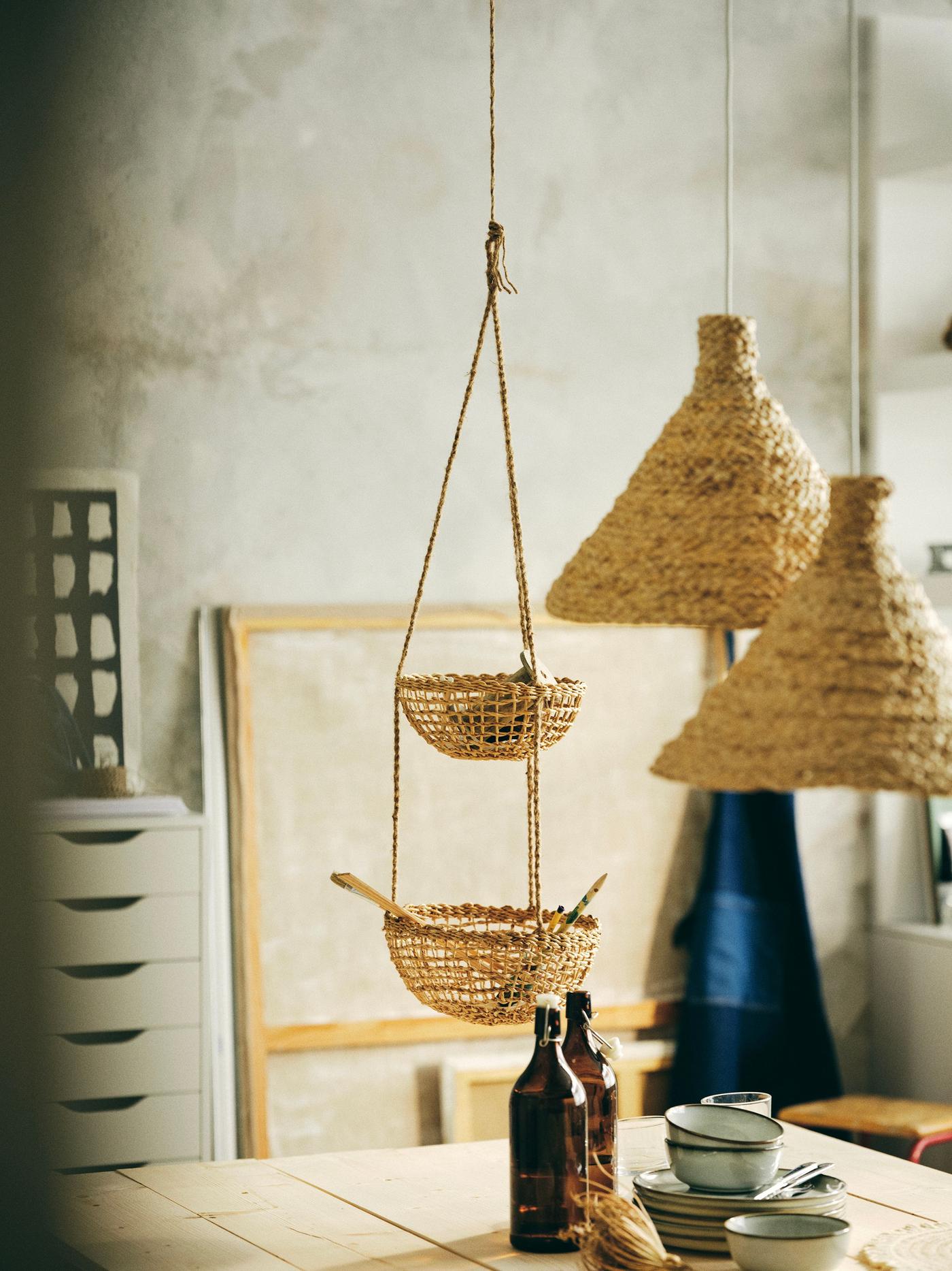 In a room with a wooden dining table, hand made lamp shade and baskets are hanging from the roof. 