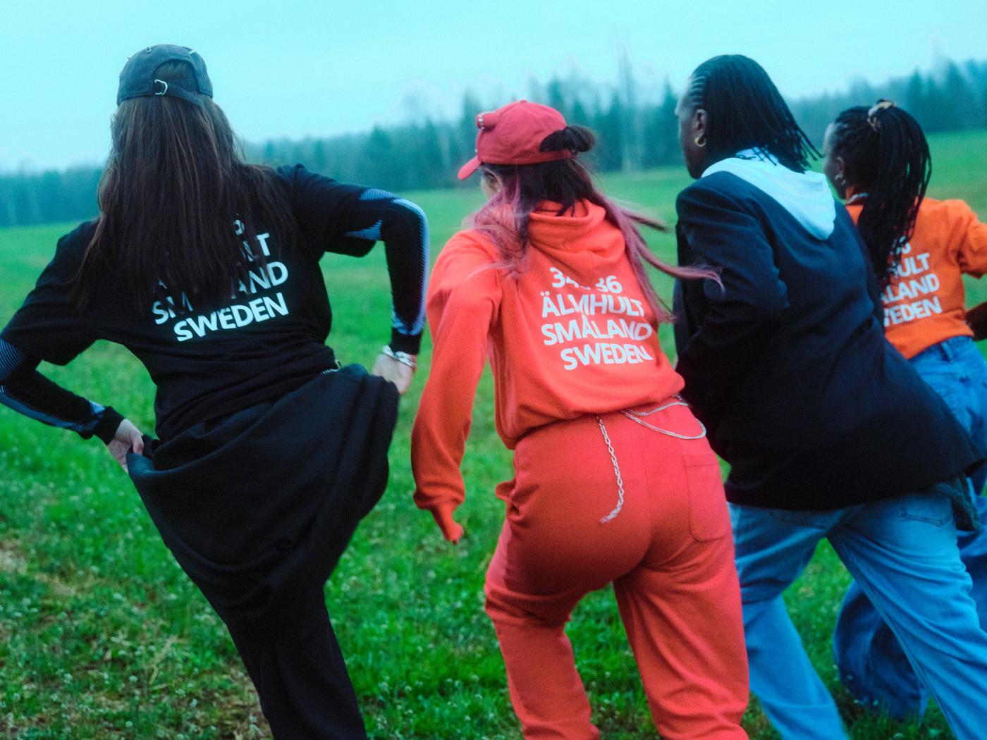 A photo of four persons running from the camera on a green field.