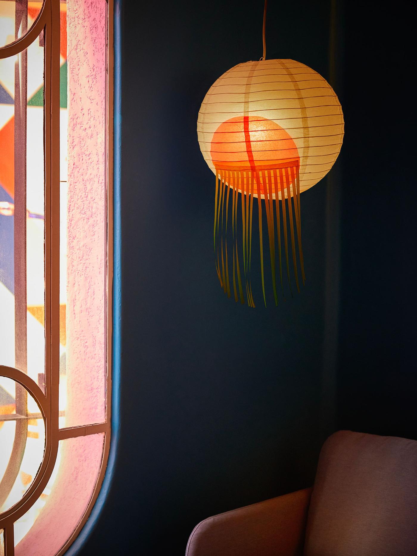 A white lampshade with red lashes hanging in a room over an armchair.