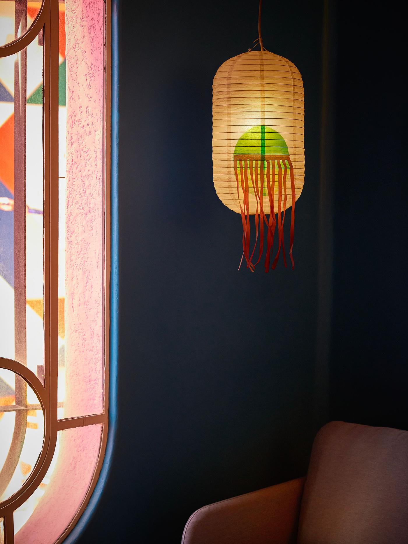 A white rice paper lampshade with red lashes hanging in a room over an armchair.