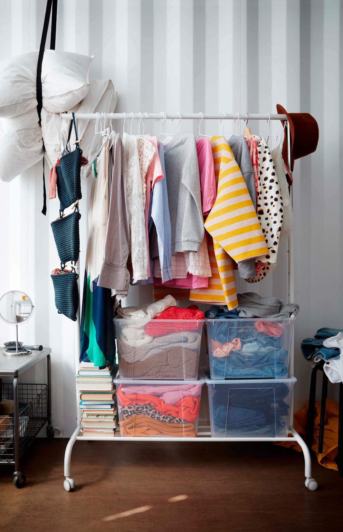 An interior showing IKEA RIGGA clothes rack with clothes in assorted colours hanging from IKEA NORDRANA hanging storage.