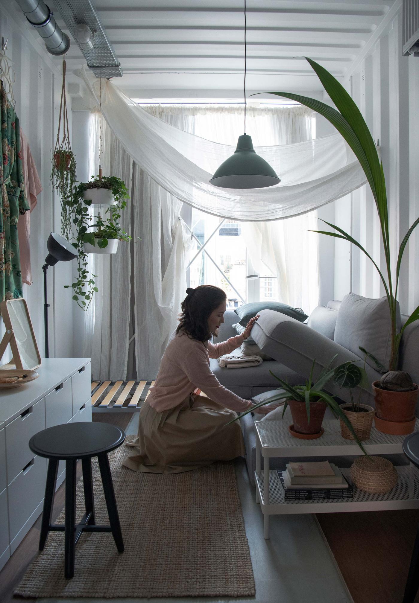 A woman sits on the floor of a living room and opens the hidden storage under IKEA VALLENTUNA modular sofa in grey.