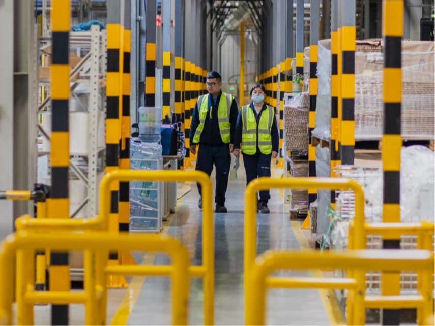 Two people in high visibility vests walking in a factory.