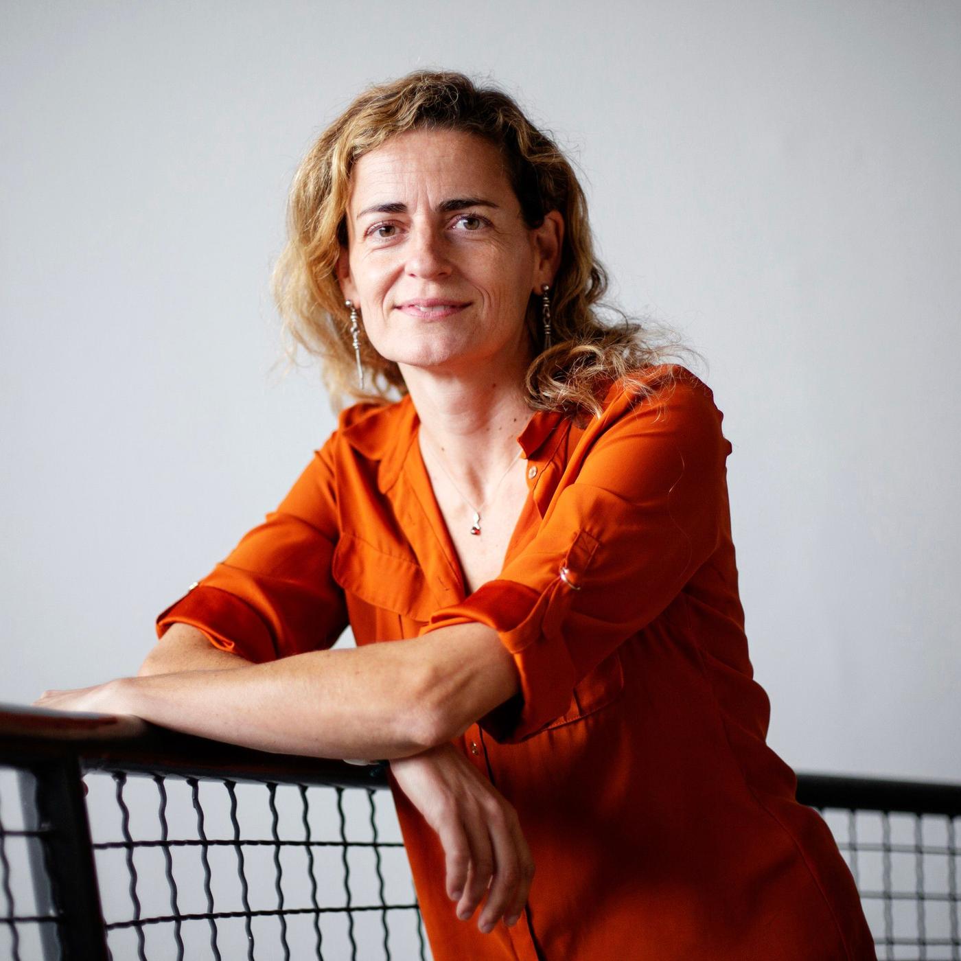 A woman with brown curly hair standing in a staircase.