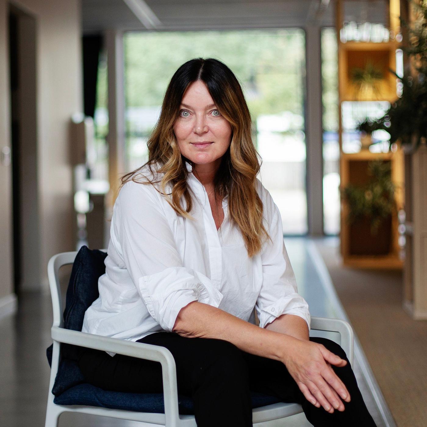 A woman in a white shirt sitting on a white chair in an office environment.