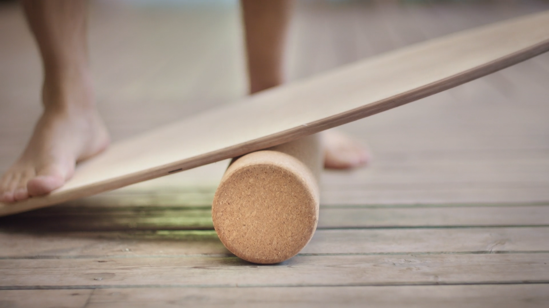 A foot rests on a wood balance board, place on a wood floor.