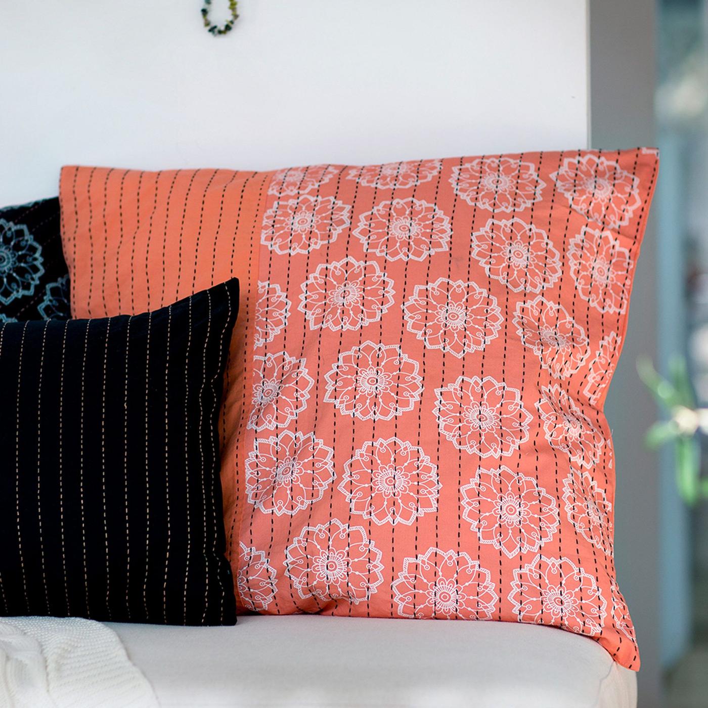 Some cushions in different sizes with hand-embroidered KRYDDGLAD cushion covers in orange, white, black and blue.