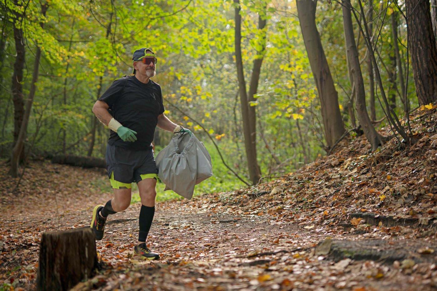 A man runs through a forest carrying a bag full of rubbish that he has collected.
