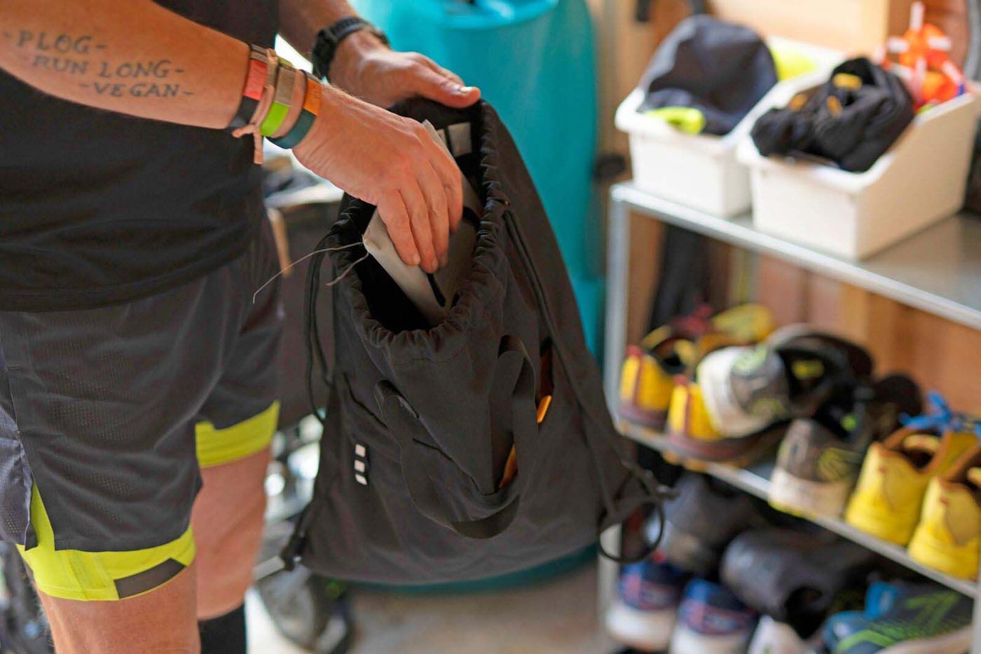 A pair of hands pack a rucksack, with stacks of running shoes in the background.