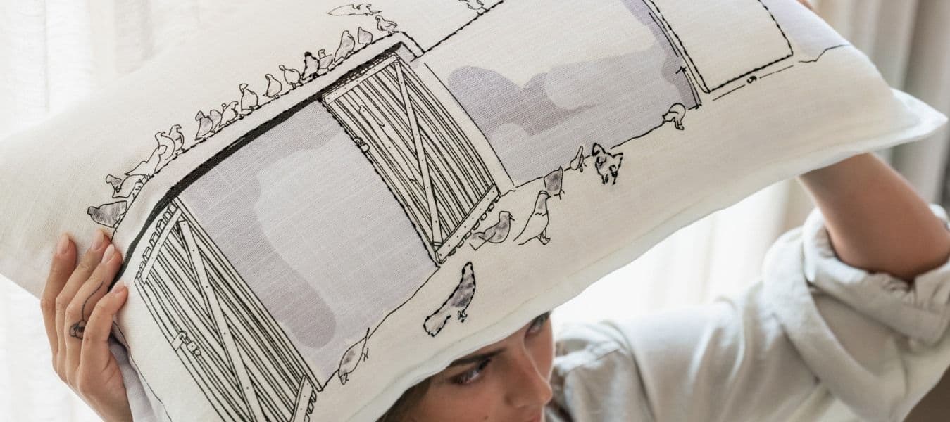 A woman is holding a large white LOKALT pillow with a black and grey decorative illustration over her head.