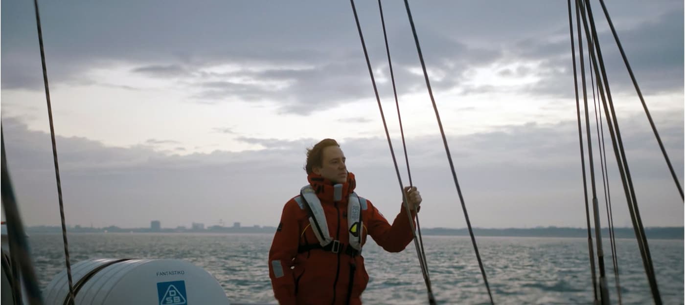 A lone sea ranger wearing a life vest on deck of a sailing ship at dawn.