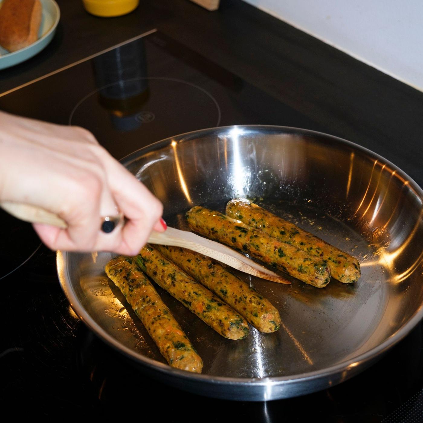 A hand stirring in a pan cooking veggie hot dogs.