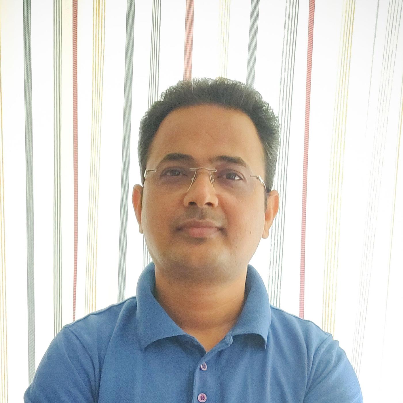 Portrait of a man in glasses and a blue shirt, in front of a striped multicolour fabric.