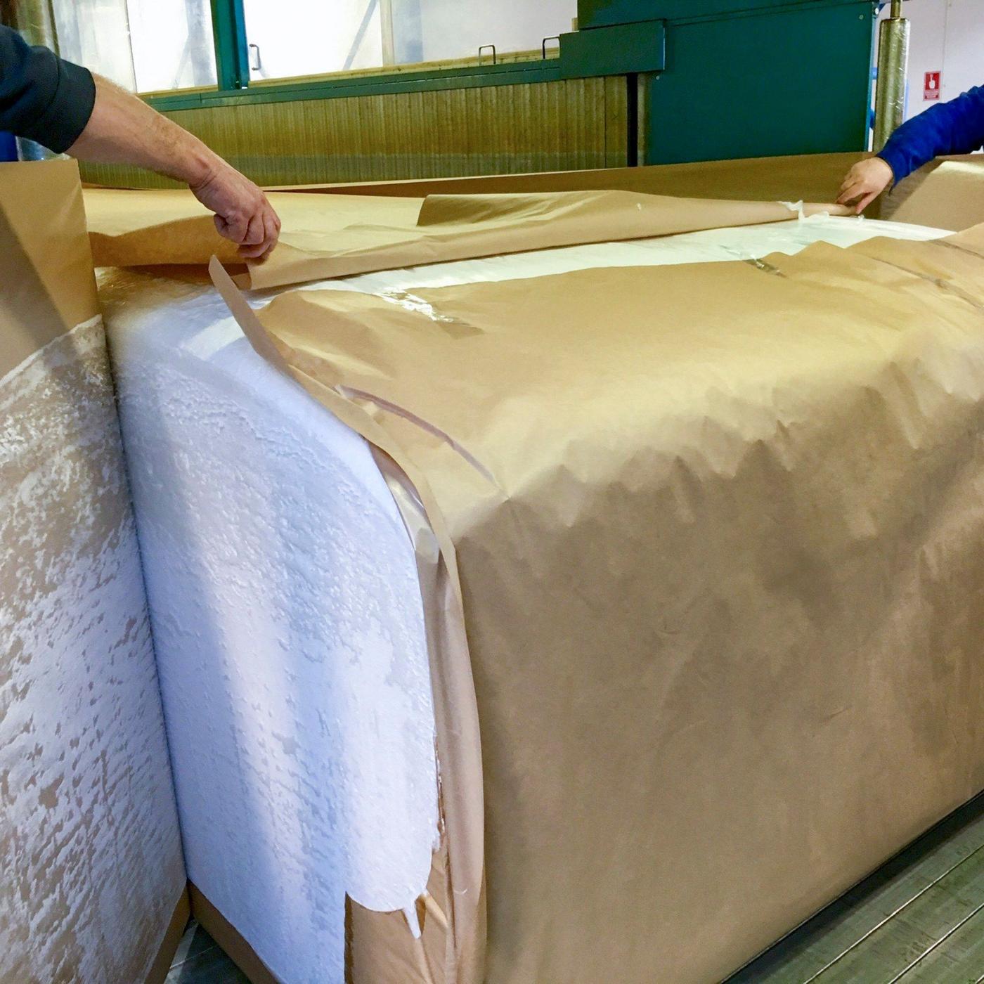 Two hands unwrapping paper from a big block of foam.