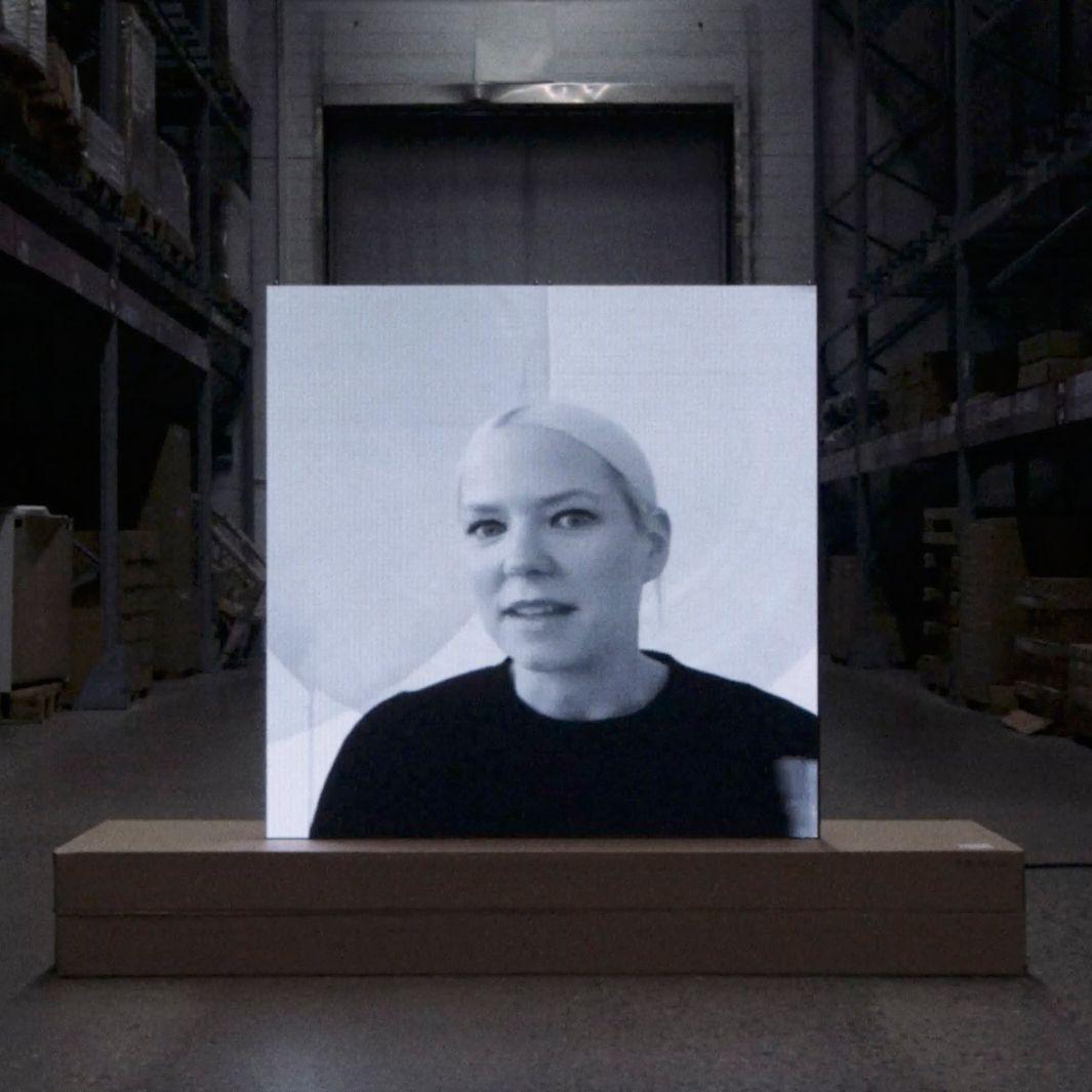 A black-and-white photo print of a blonde woman in a dark sweater, on a brown base in a dark warehouse.