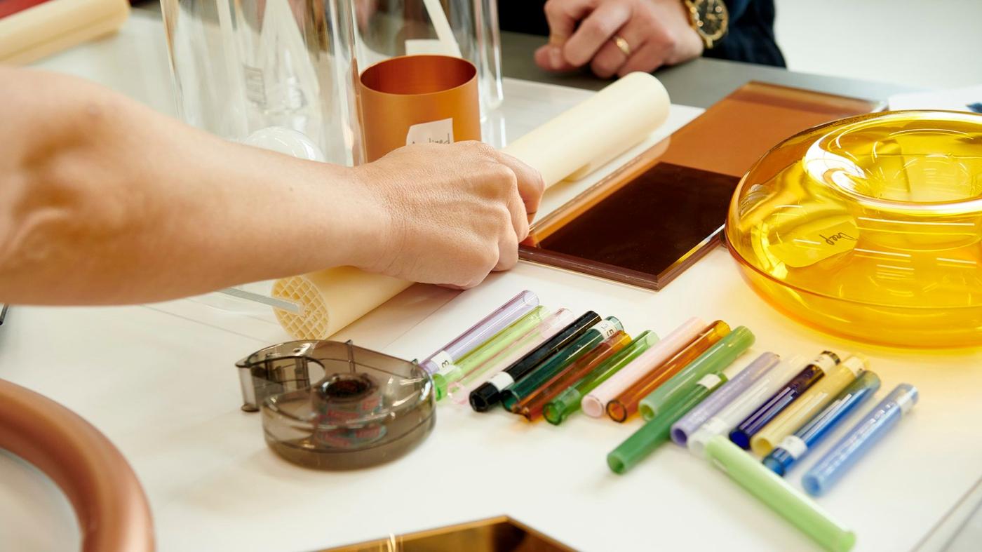 A hand holding a plastic tube, laying on a desk together with pens and product samples.