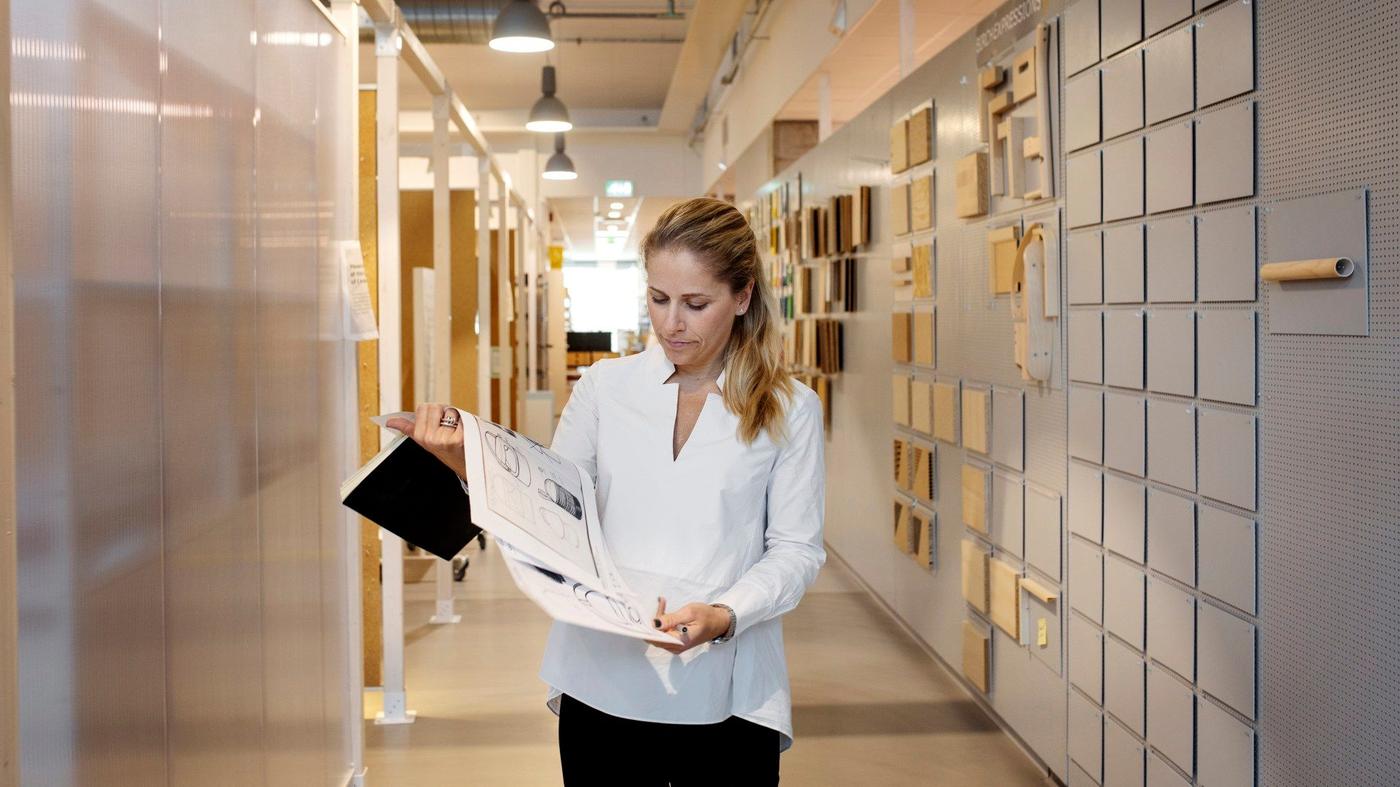 A woman in a white shirt standing with sketches in her hand