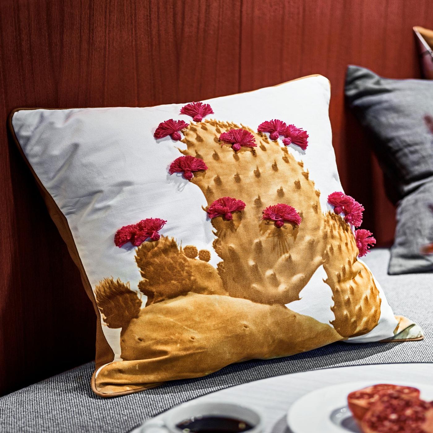 A cushion with a white TILLTALANDE cushion cover with a hand-embroidered, golden yellow cactus with red flowers.